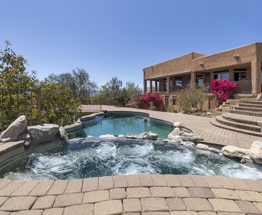 Luxury residential pool with a heated spa, surrounded by landscaped gardens and a view of the desert, emphasizing ideal swimming conditions and automation system integration for optimal maintenance.
