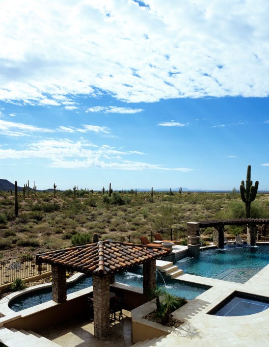Desert landscape featuring a luxurious pool area with a stone gazebo, surrounded by cacti and greenery, under a bright blue sky, representing the outdoor oasis services offered by Luna Pool Service.
