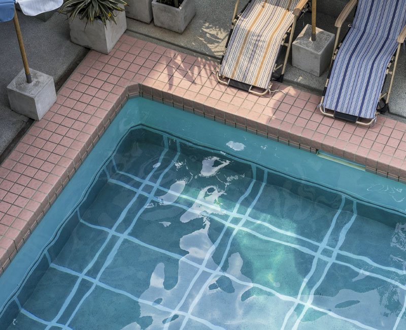Swimming pool with visible tiled surface and clear water, surrounded by a patio area featuring two lounge chairs, illustrating a well-maintained pool environment relevant to professional pool inspections by Luna Pool Service.