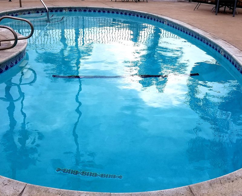 Clear swimming pool with visible reflections, featuring coping and railings, highlighting the importance of visual pool inspections for maintenance and safety compliance.