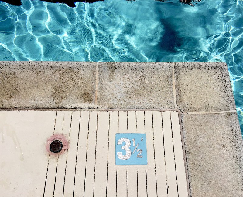 Poolside view showing depth marker of 3½ feet, with clear blue water reflecting sunlight, emphasizing the importance of safety in pool inspections.