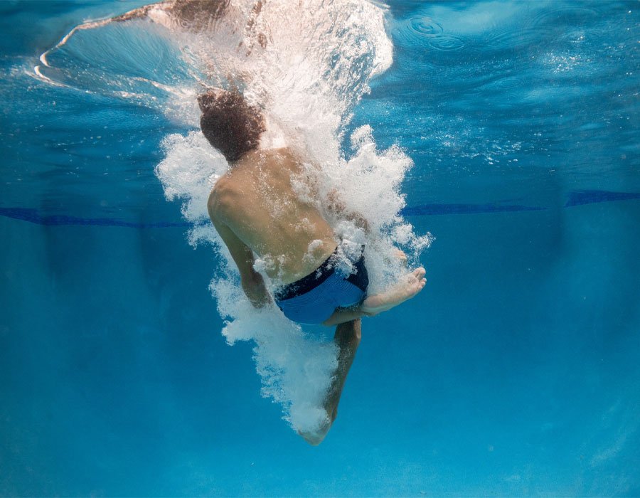 Child diving into a clear swimming pool, creating splashes, emphasizing safe and enjoyable swimming environment for pool maintenance and testing services.