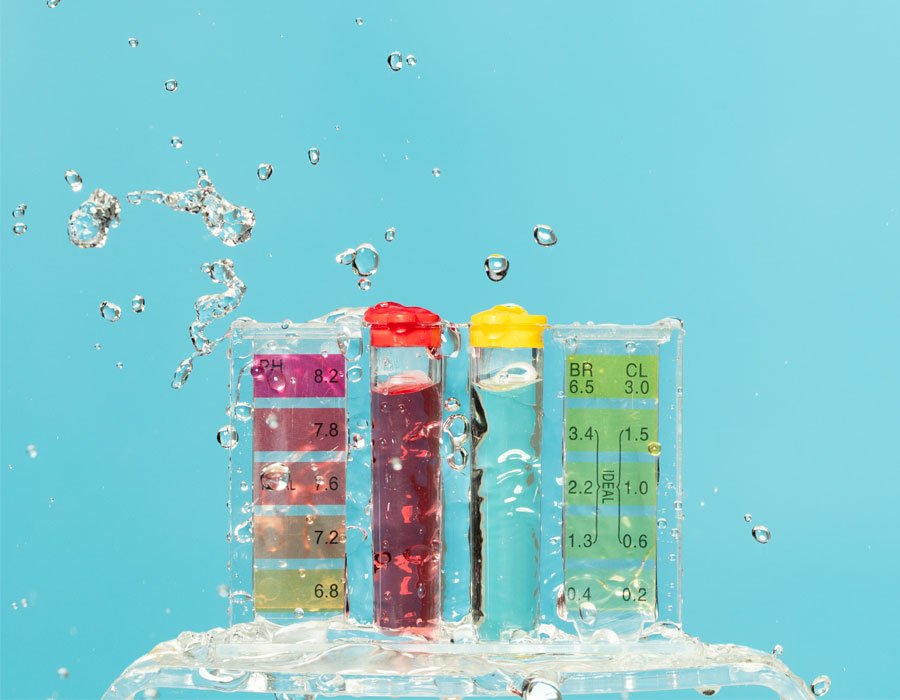 Pool water testing kit with color-coded vials displaying pH and chlorine levels, surrounded by splashing water, emphasizing pool water quality and safety.