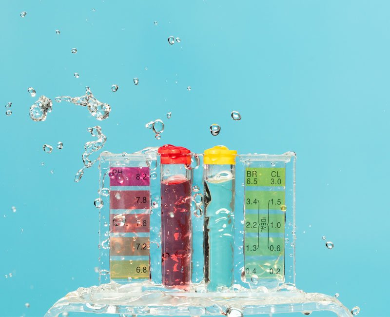 Testing vials with colorful liquids and water splashes, representing pool water chemistry analysis for maintenance and safety.